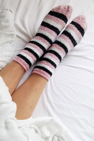 A woman's sock covered feet poke out from the covers at the end of her bed