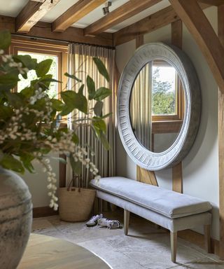 Small hallway with upholstered bench and large mirror above with neutral walls and floor