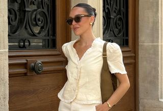 Influencer Emma Leger wearing cream Reformation top with sunglasses and brown suede bag and standing on Paris street.