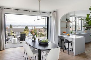 Bifold doors open in dining area with black table and white chairs and white island and black stools wide view from window and patio furniture