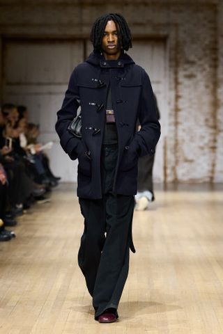 A model walking in Coach's Fall 2025 runway show in a navy duffel coat.