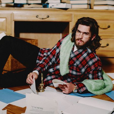 Andrew Garfield for Who What Wear's September cover wearing a plaid button-down with a green sweater over his shoulders, black pants, and white shoes.