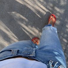 A woman walking in jeans and red flip flops with a black pedicure