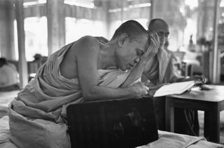 Black and white photo of a Buddhist monk in a temple resting his head in his hand.