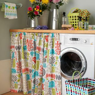 Wooden worktop with washing machine underneath, and a patterned curtain instead of a door