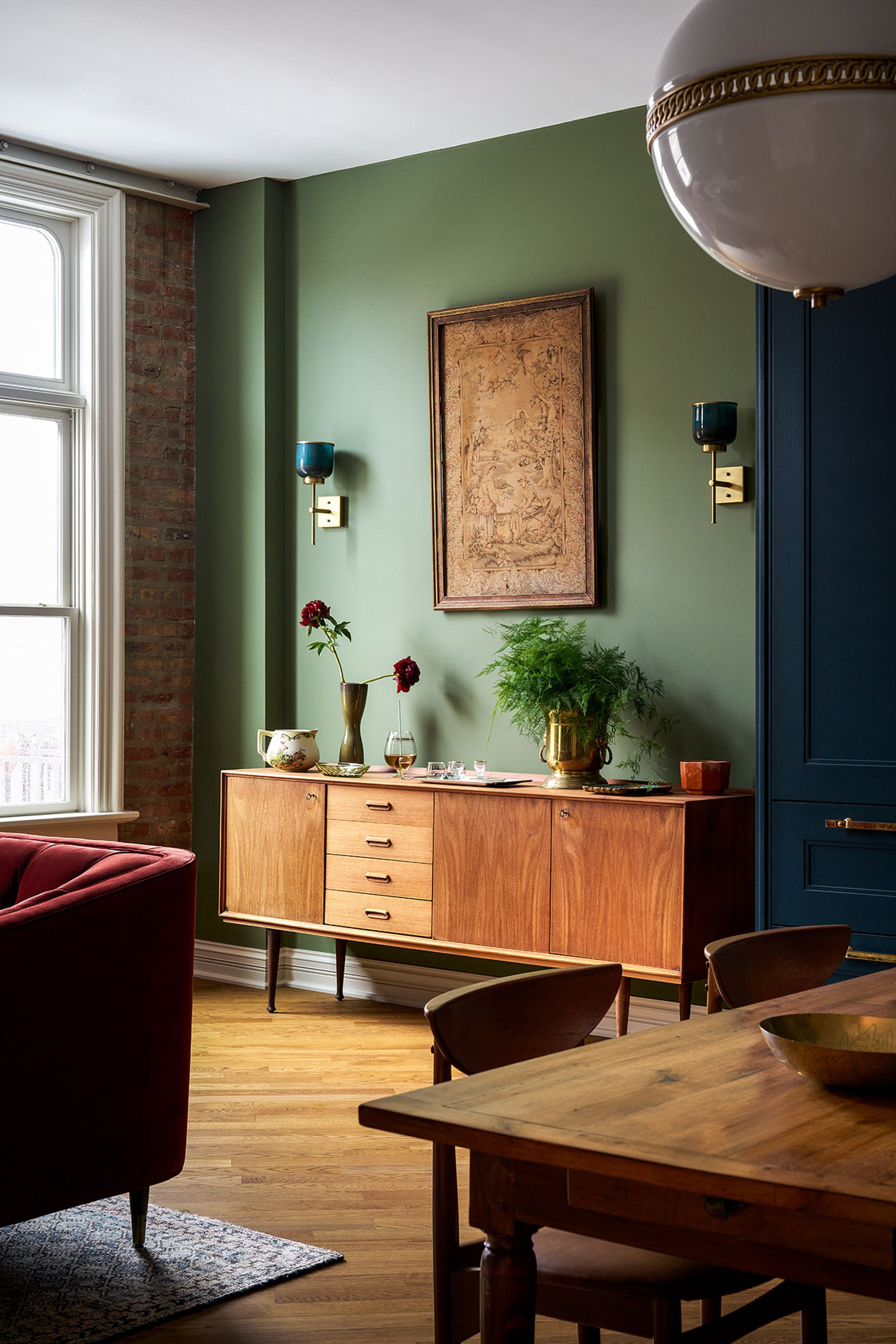 Wooden sideboard table against a muted green wall. There are golden fixtures and bare brick to add ambience 