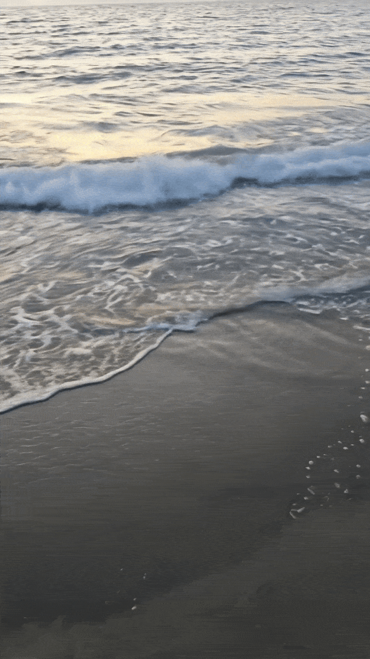 Waves lapping on the beach in front of a sunset