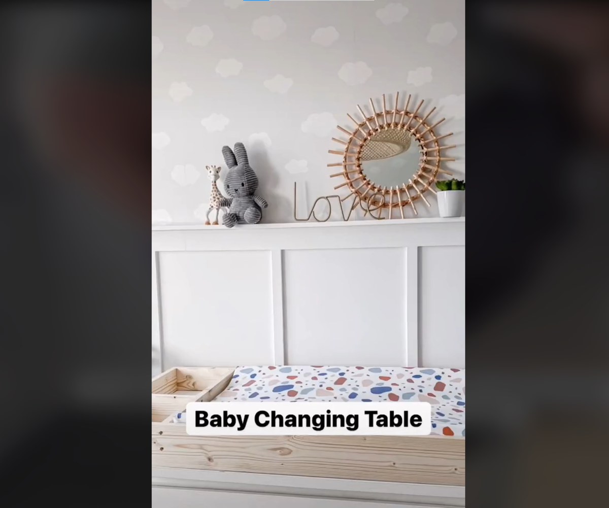 DIY baby's changing table made of wood and painted white sitting underneath shelving with children's toys