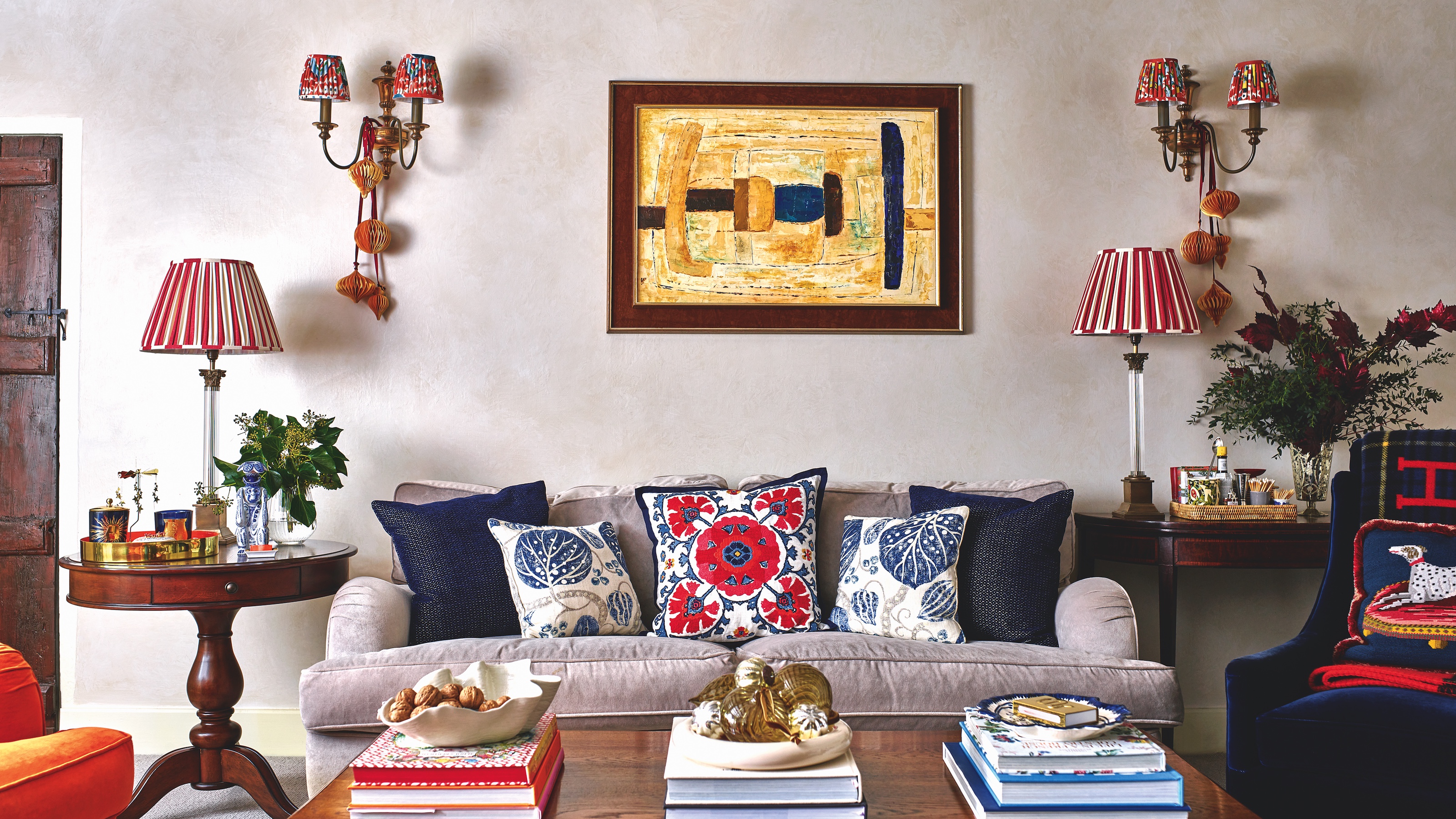 living room with sofa covered with cushions, wooden coffee table piled with books, and David Hunt wall lights
