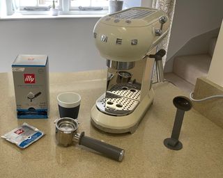 A cream Smeg coffee maker on countertop with Illy decaffeinated coffee pouches