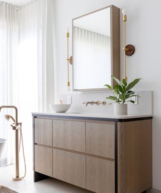 A white bathroom featuring a gray wood vanity with a white countertop and backsplash. Above, a matching wood vanity mirror is framed by two gold wall lights