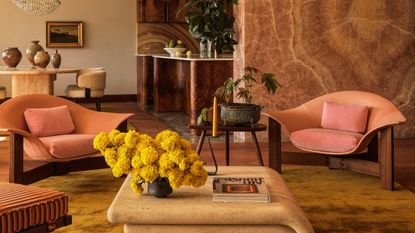 a living room with a beige carpet, stone wall, burl wood kitchen, and stone backsplash, that all sort of clash in a way