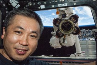 Japan Aerospace Exploration Agency astronaut Koichi Wakata poses for a photo at a window in the Cupola of the International Space Station while the Canadarm2 robotic arm's Latching End Effector appears to be looking through the window from outside the station.