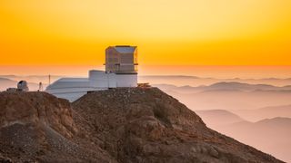 A metal building with a large dome sits on a rocky cliff
