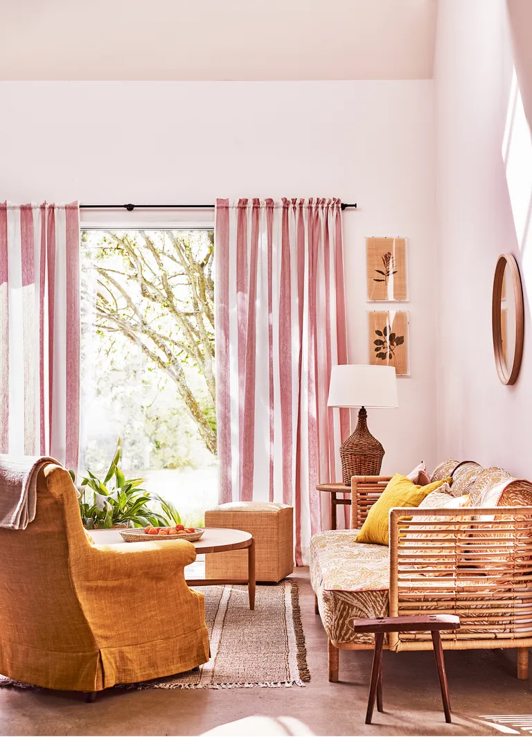 Airy living room with wicker furniture, rattan lamp and pink and white striped curtains in front of large french windows
