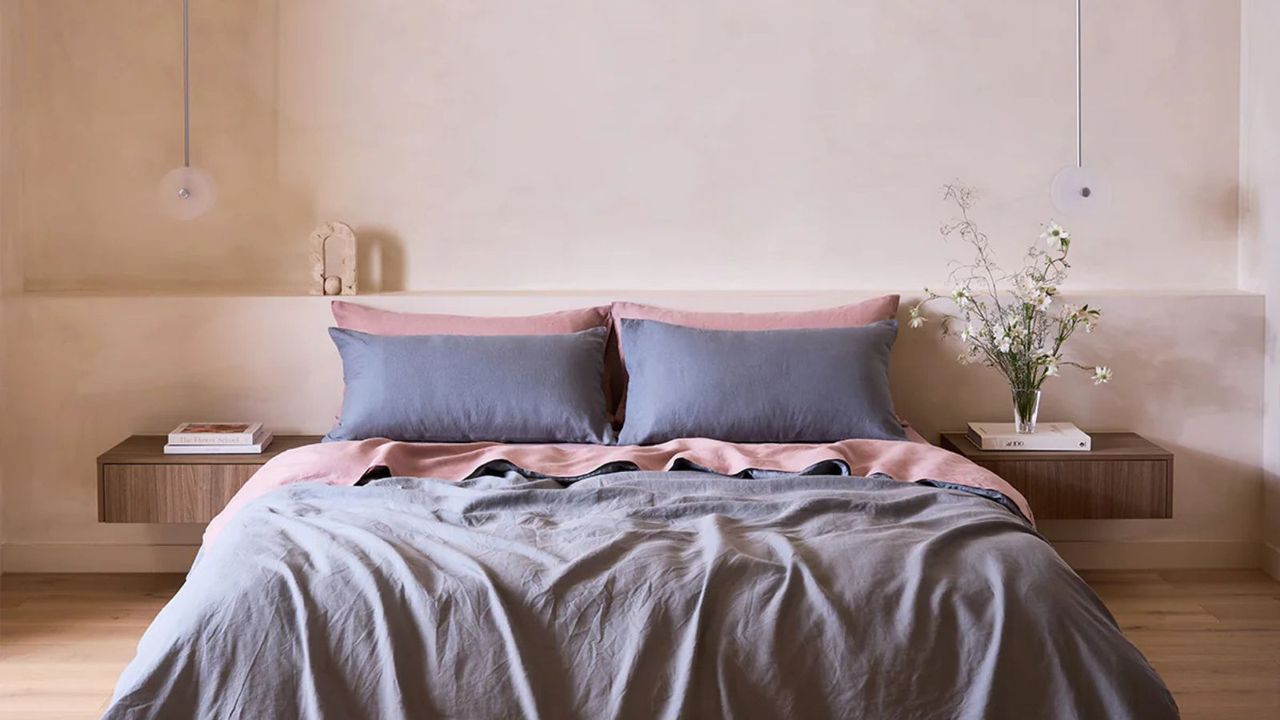 Lavender and pink linen sheets on a bed against a cream wall. 