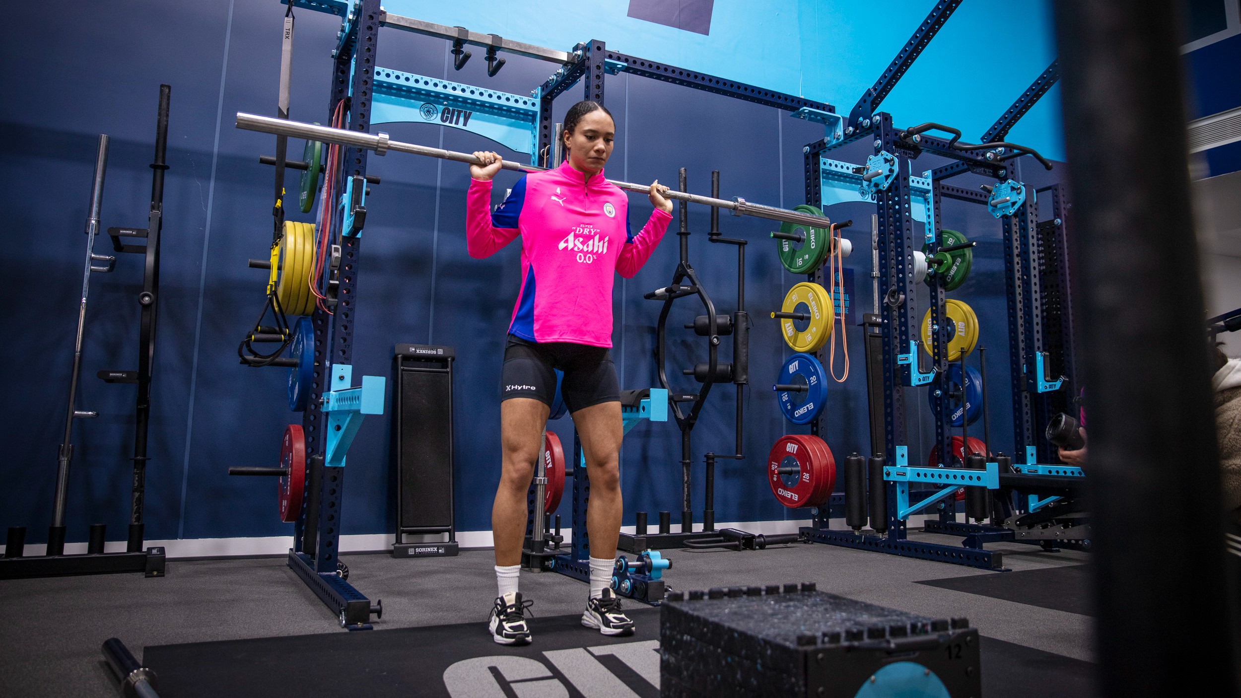 Female Manchester City player training in the gym with a barbell over her back for a squat