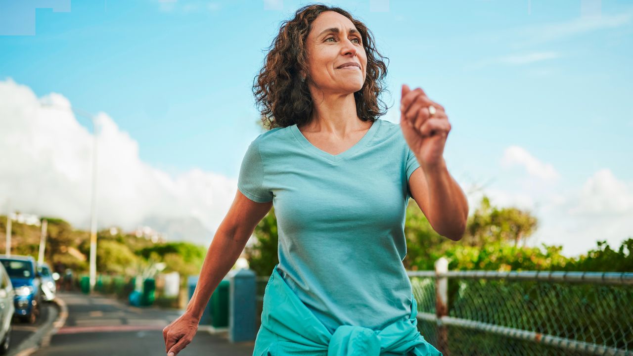 Smiling woman walking next to road. There is a blue sky in the background