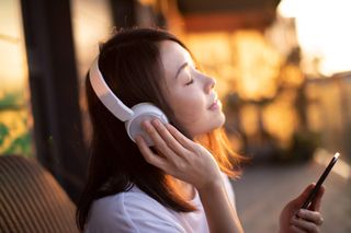 A woman listening to music while sat outside in the sun.