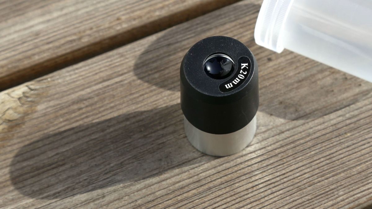 The silver and black eyepiece of a telescope sits on a wooden surface.