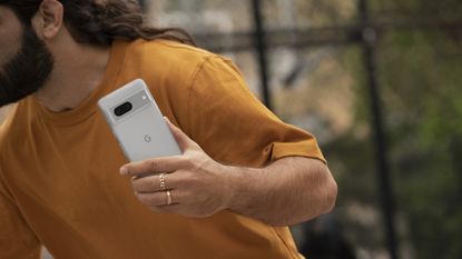 Google Pixel 7 review: man in orange tshirt holding white phone