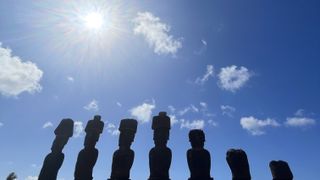 the sun in the sky above a row of moai statues.