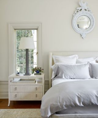 calming bedroom with cream walls, white nightstand and white and gray bedding