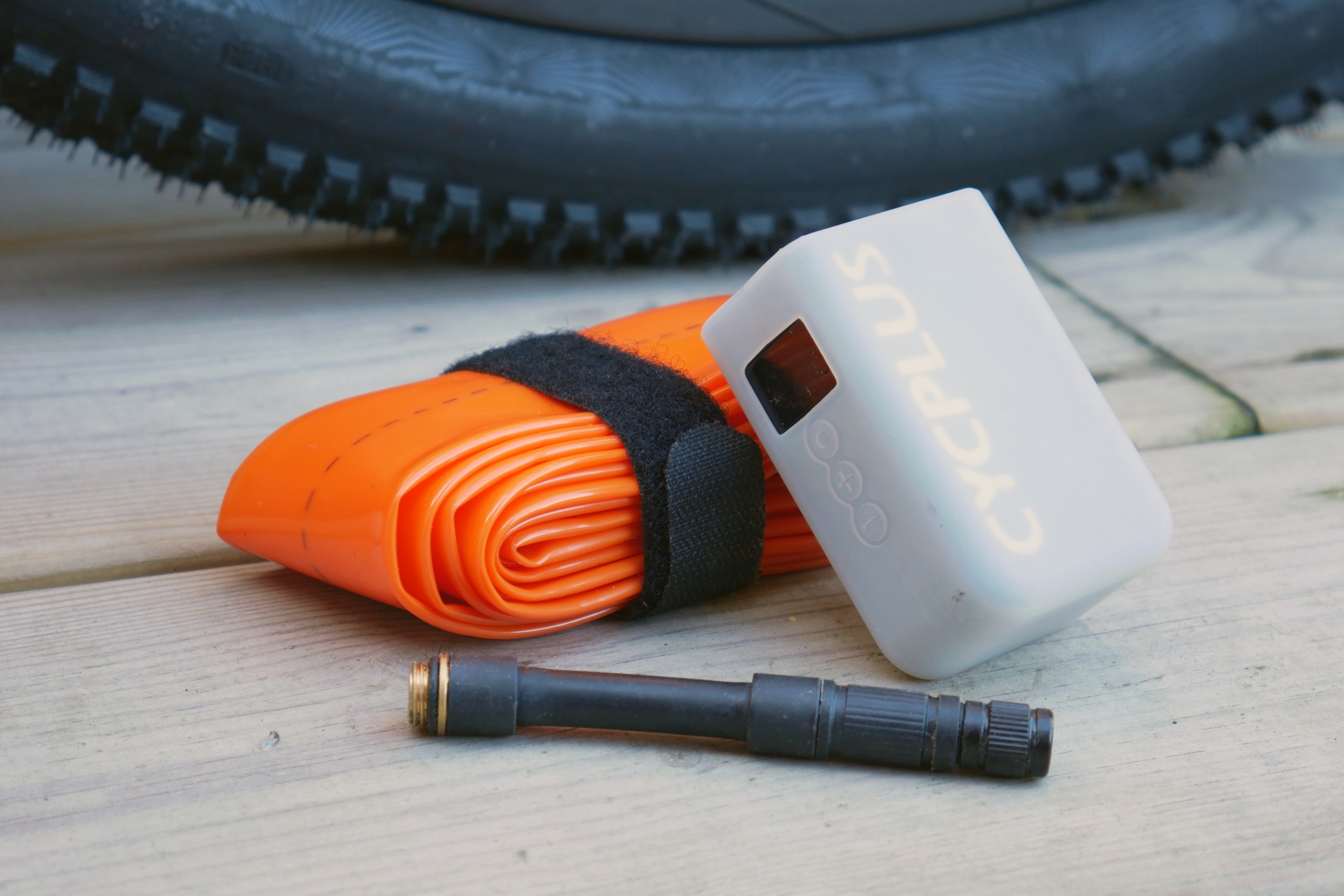 A tubolito TPU inner tube and Cycplus AS2 Ultra electric pump with its valve extension placed on a wooden deck, with a gravel tyre in the background