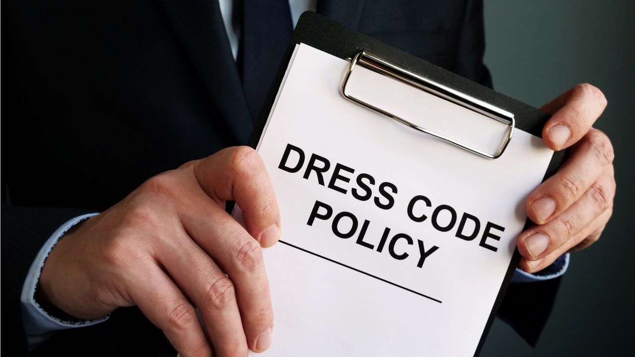 A businessman holds a clipboard with a paper that says Dress Code Policy.