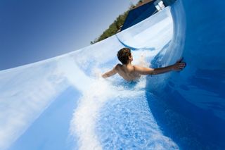A boy goes down a blue water slide at a water park on a sunny day