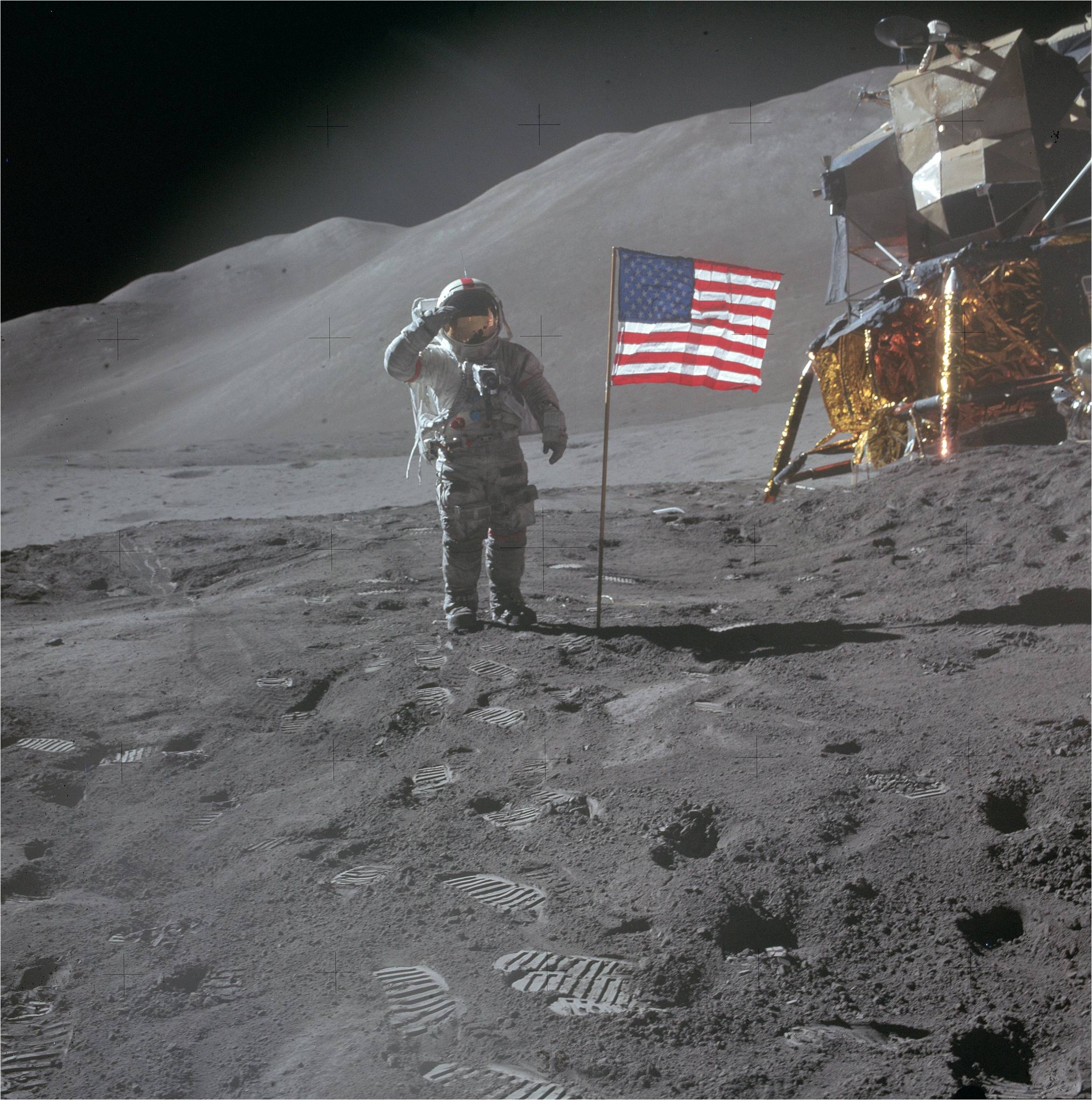 an astronaut in a bulky white spacesuit plants an american flag on the dusty grey surface of the moon