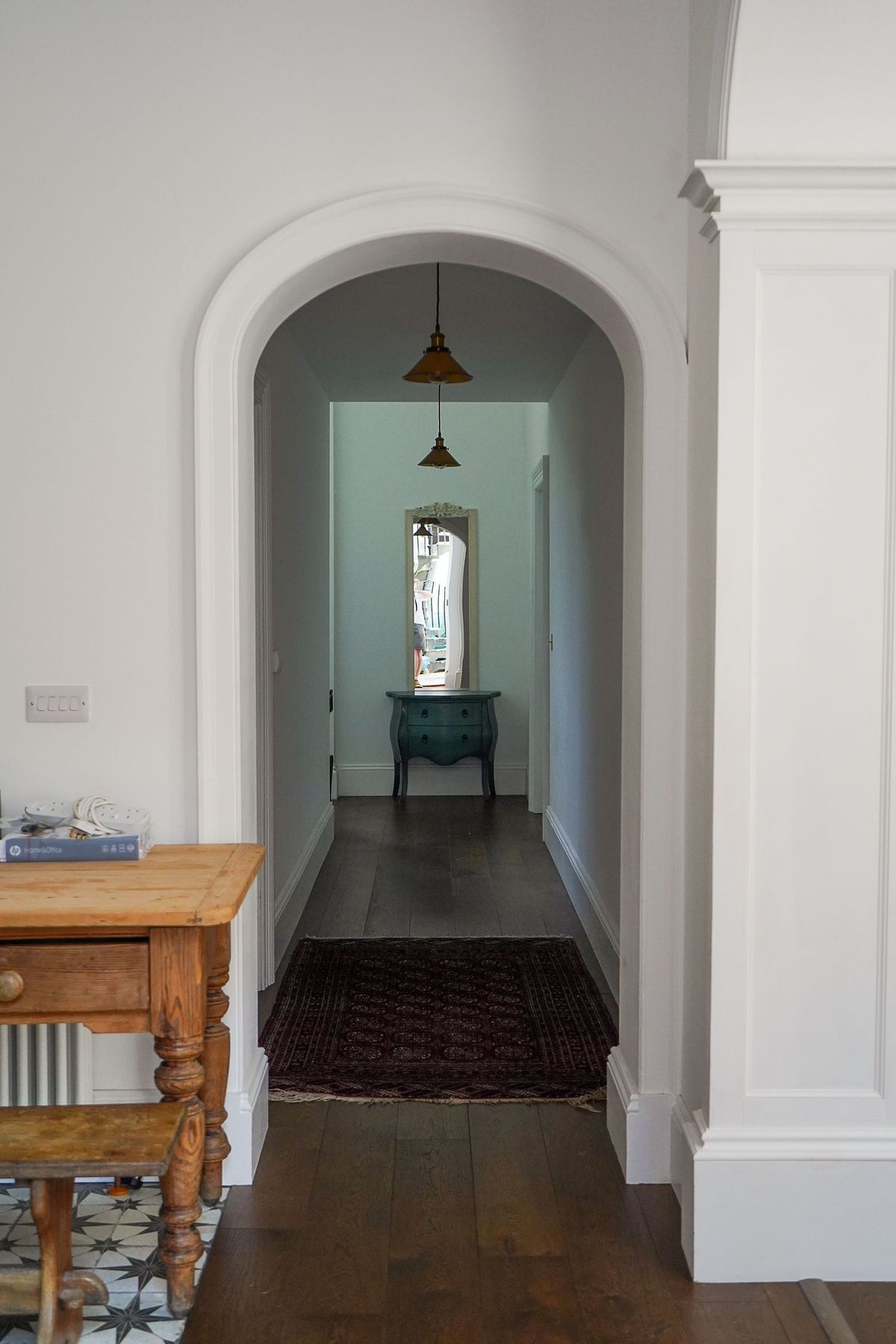 An arched hallway with green feature wall at the end and wooden flooring