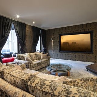 cinema room with big tv screen and sofa with cushions and glass table