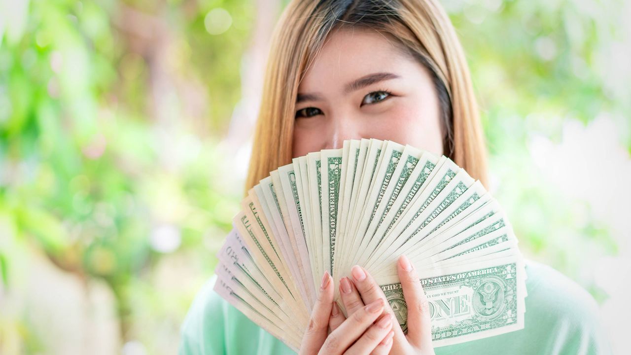 A teenage girl holds a fan of $1 bills.