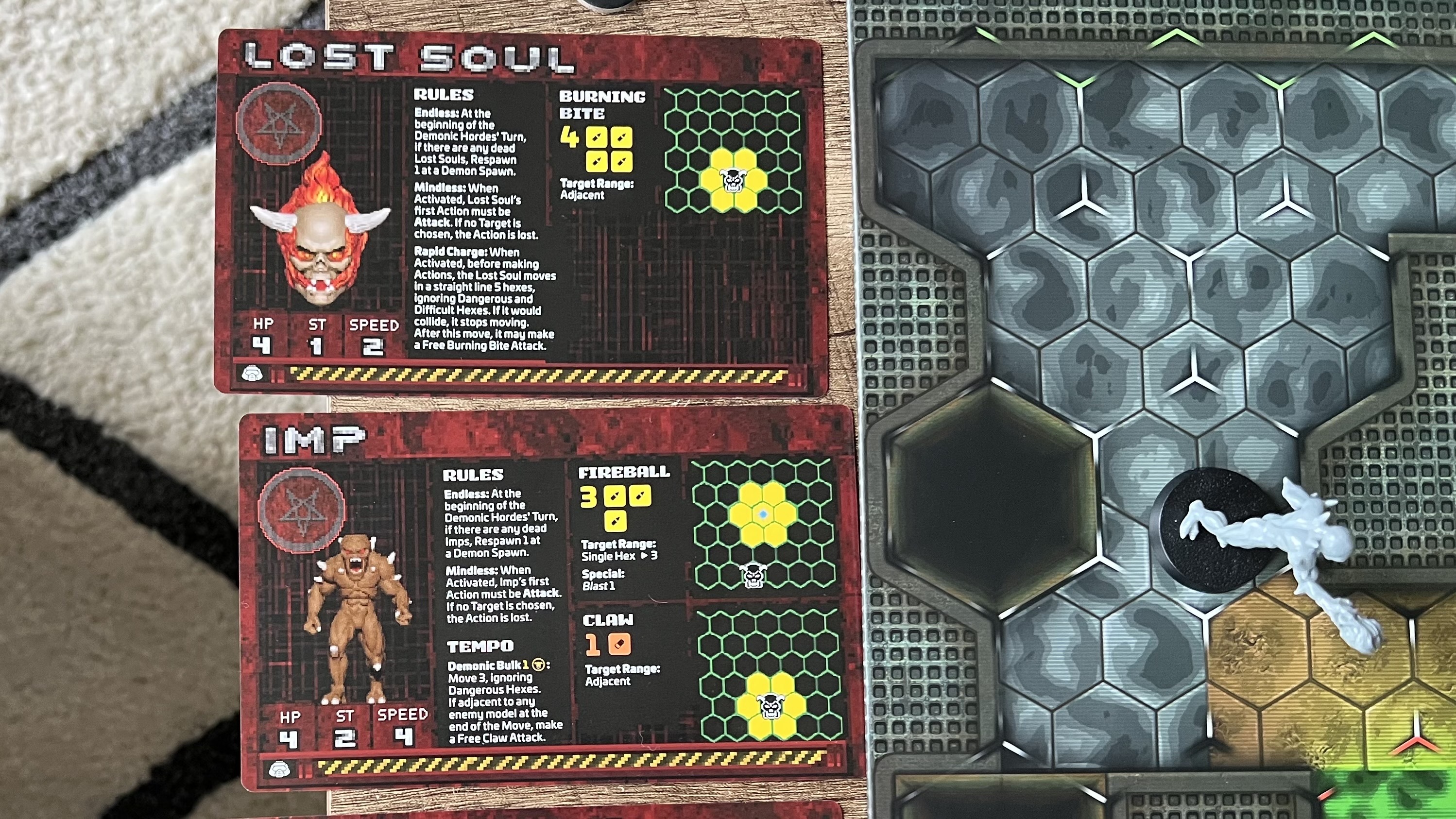 Top down view of demon character cards next to a map board in Doom Arena Board Game