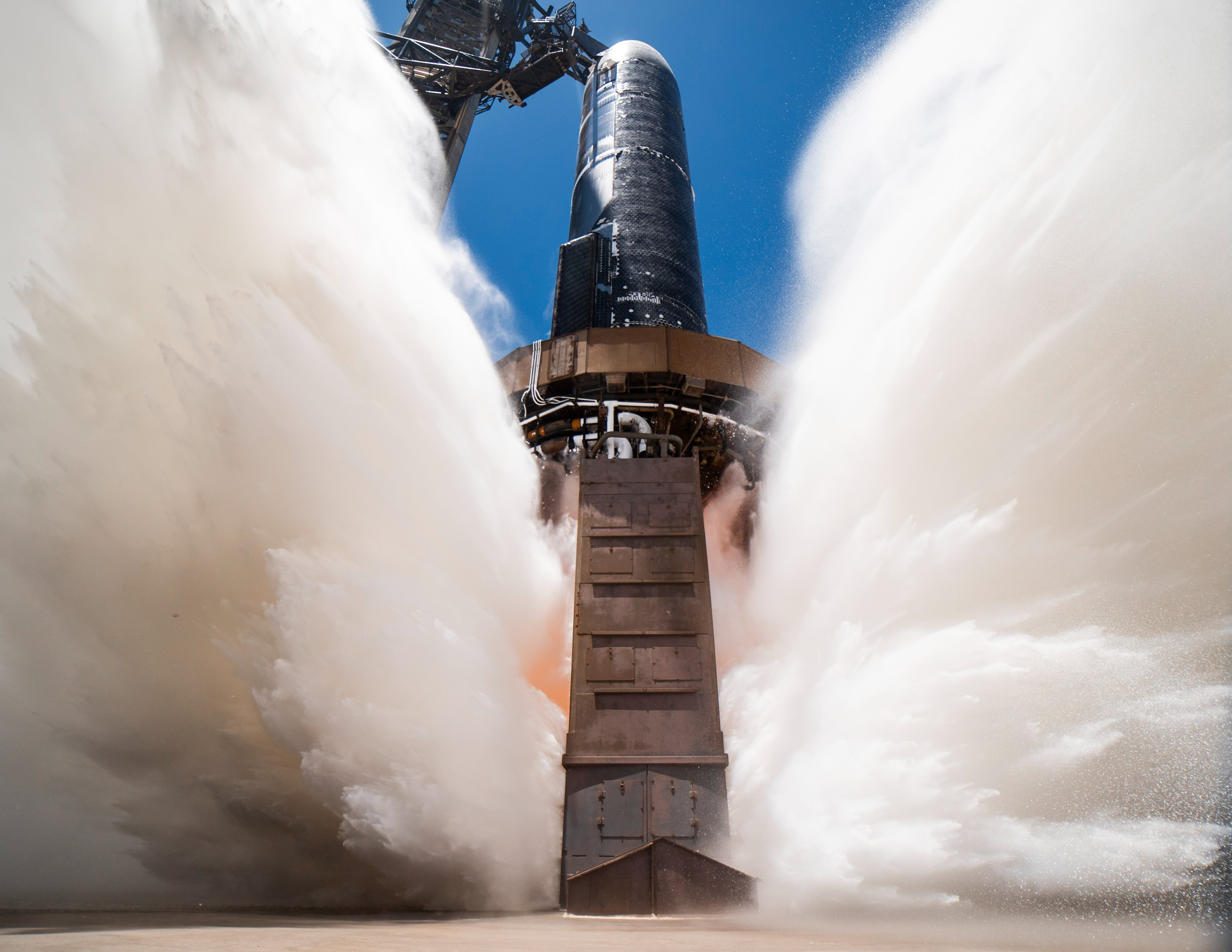 view of a rocket engine test from below, with water spraying all around it