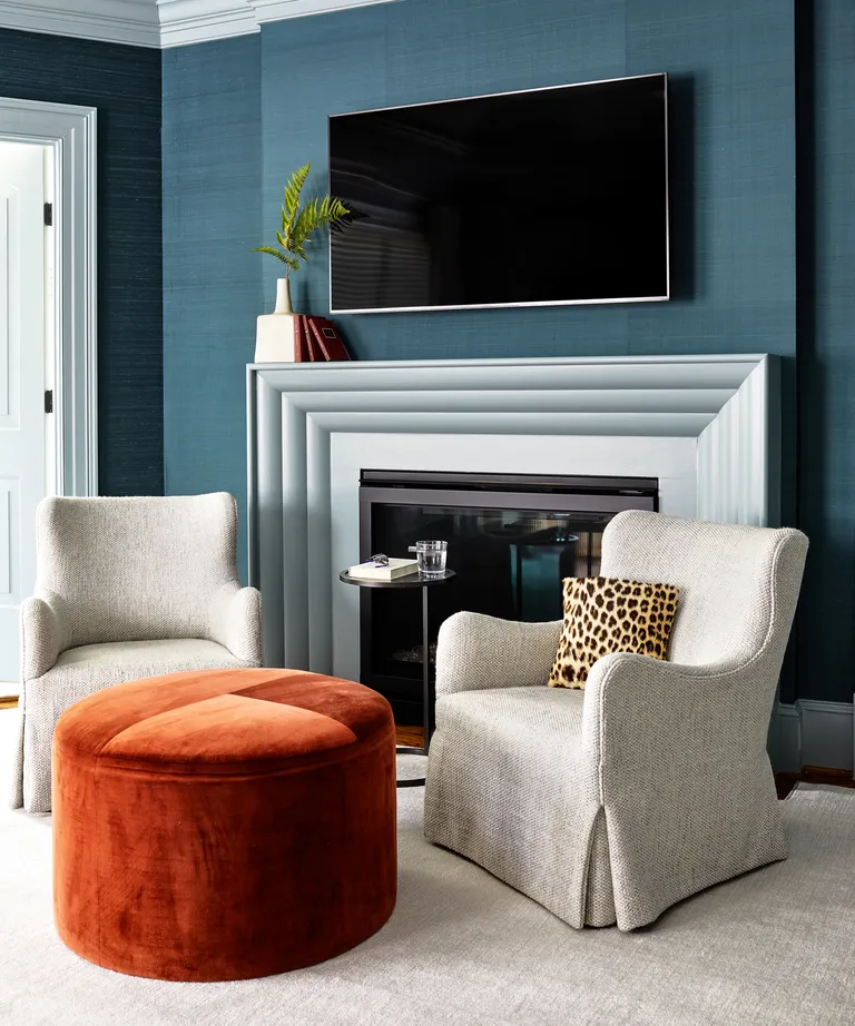 A bedroom with blue walls, two white armchairs and an orange velvet storage ottoman