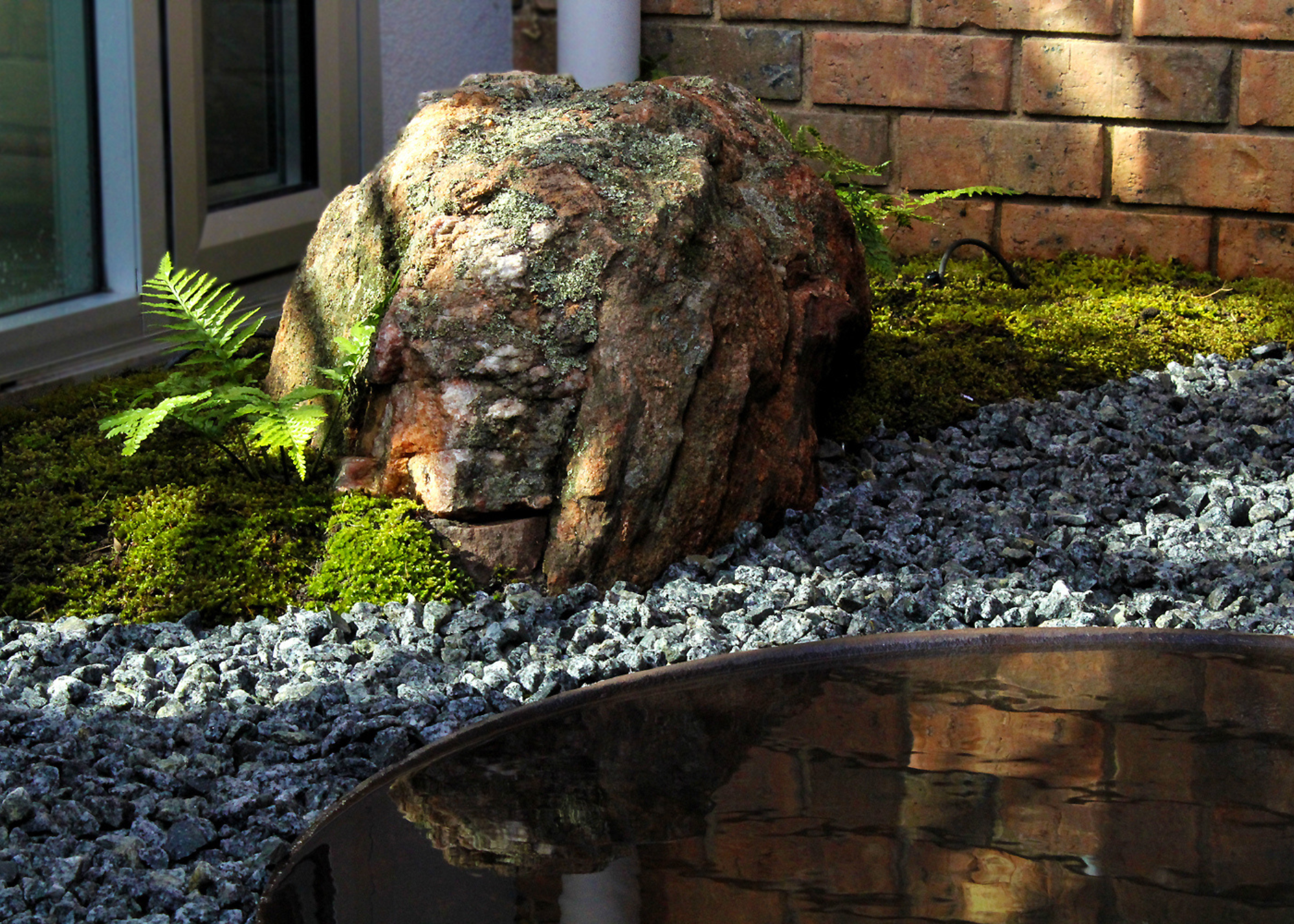 A moss and rock garden with ferns and a vessel of water