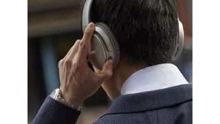The back of a suited man wearing Bose QC 25 on his head.
