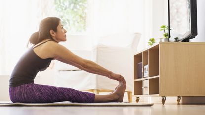 Woman stretches on exercise mat while looking at TV in domestic setting
