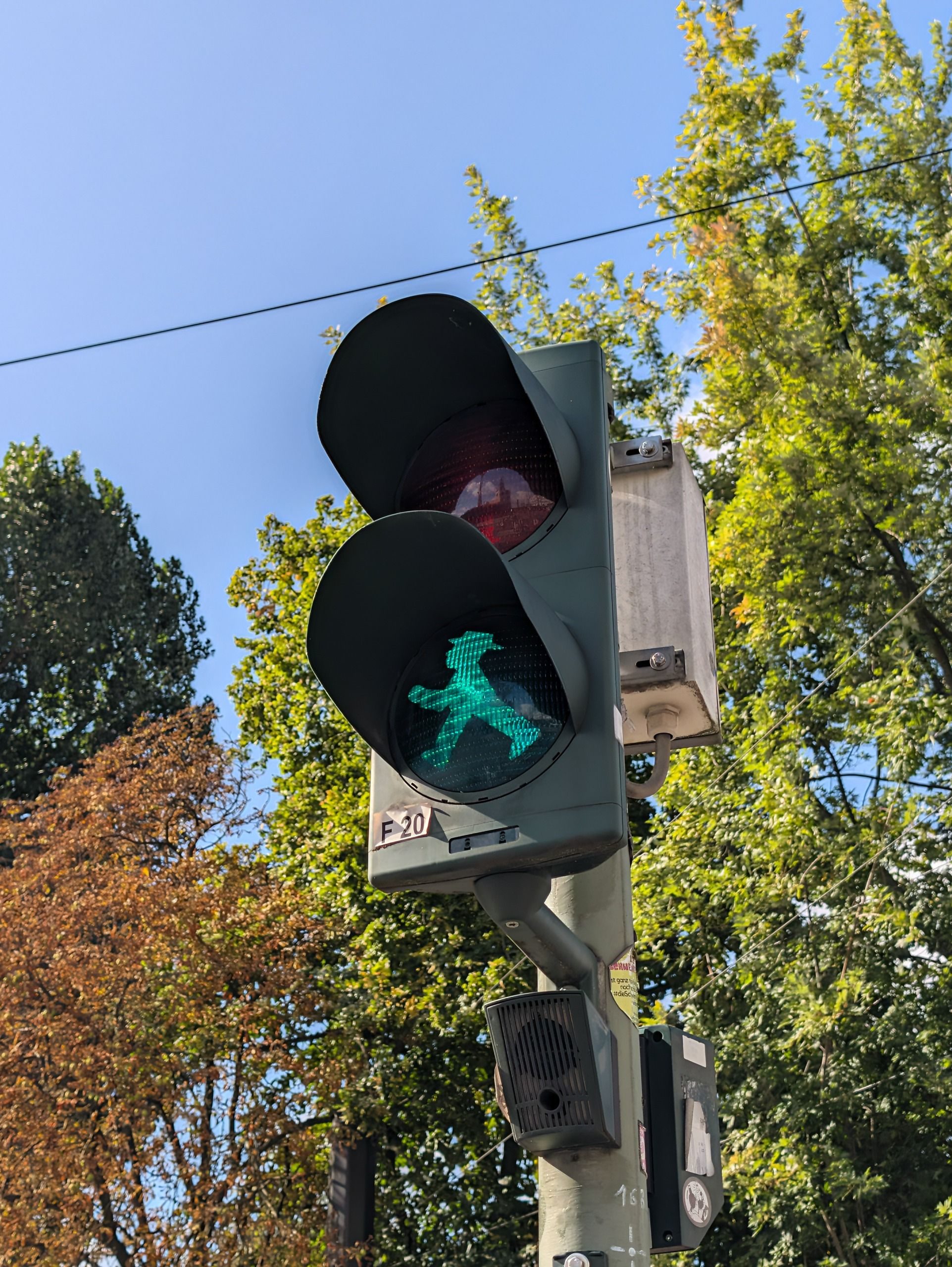 Berlin pedestrian crossing light showing the green Ampelm&auml;nnchen walking figure against leafy trees.