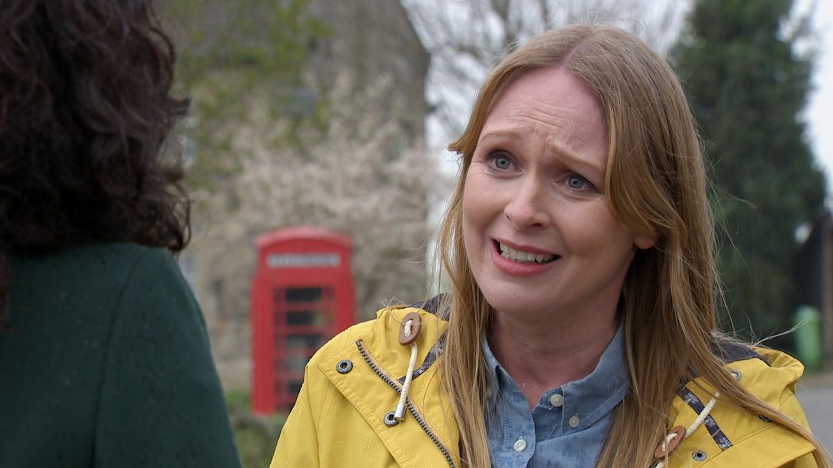 Vanessa looking sad, standing outside in the Emmerdale village and wearing a yellow coat. 