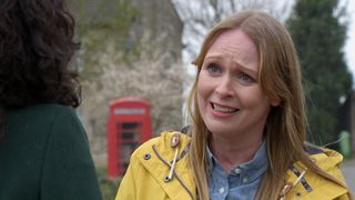 Vanessa looking sad, standing outside in the Emmerdale village and wearing a yellow coat. 