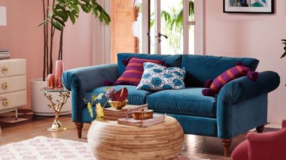 Anthropologie sales - a colorful living room with a blue couch and cushions against a light pink wall.