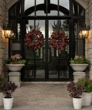 large glass contemporary arched front door with two dark red wreath and potted plants