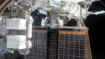 two astronauts wearing white spacesuits work outside of a space station "above" a pair of solar array panels