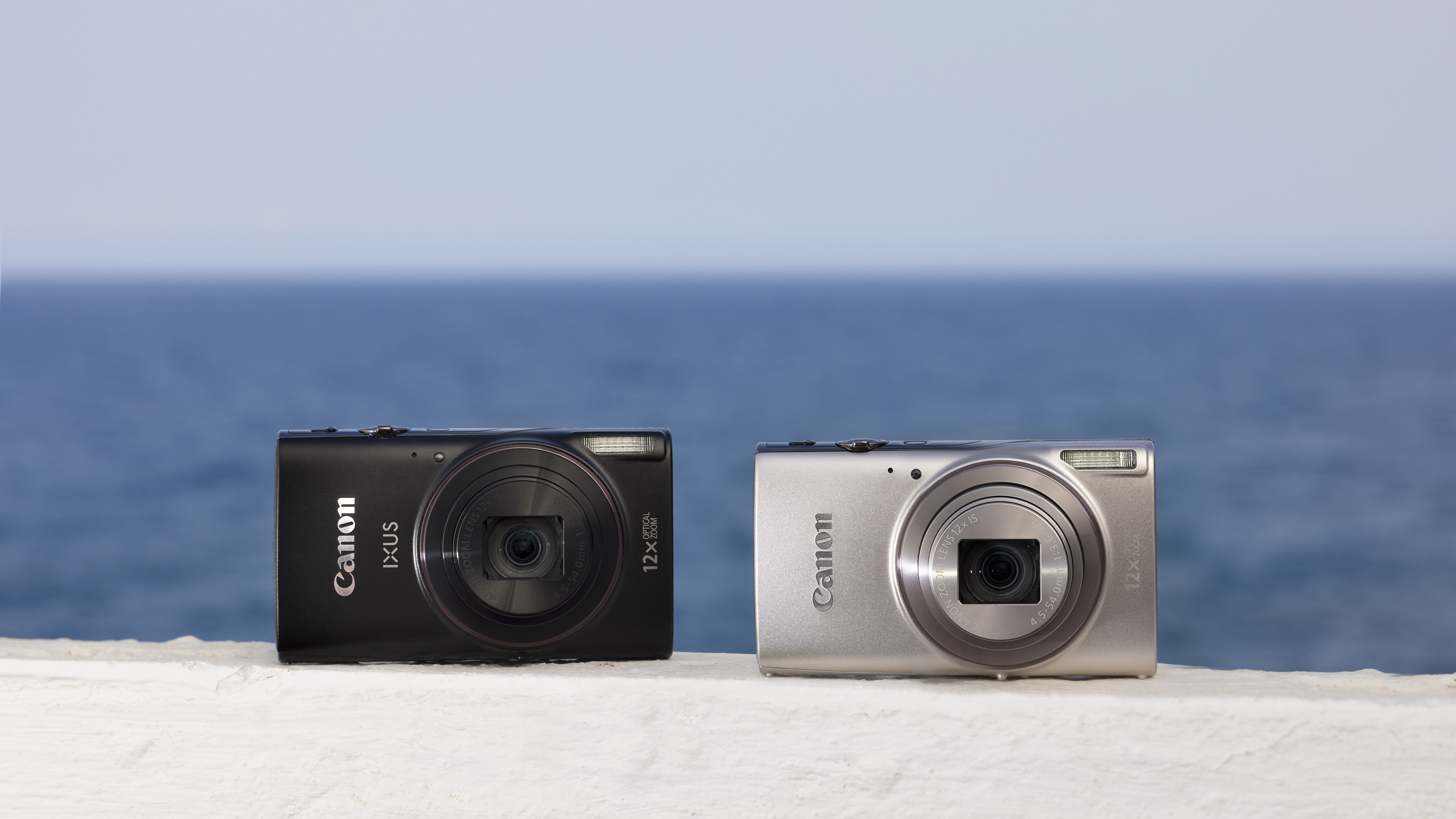Canon PowerShot Ixus 285 HS A black and silver in front of a shoreline