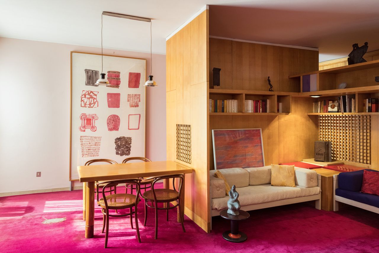 Compact apartment design with dinning table &amp; chairs, two couches, wall shelving, coffee table and a pink carpet.