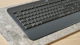 a black full sized keyboard with batteries and a palm rest on a clean beige surface with a blue backdrop