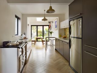 A kitchen extension with parquet flooring, a range cooker opposite a fridge and a dining area next to glass bifold doors